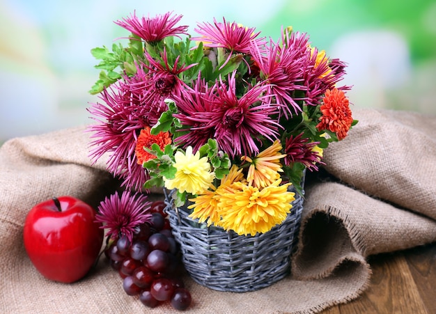 Composición con hermosas flores en florero de mimbre y frutas, sobre fondo brillante
