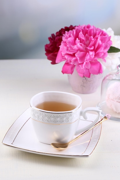 Composición de hermosas peonías en jarrón, té en taza y malvavisco, sobre mesa, sobre fondo claro