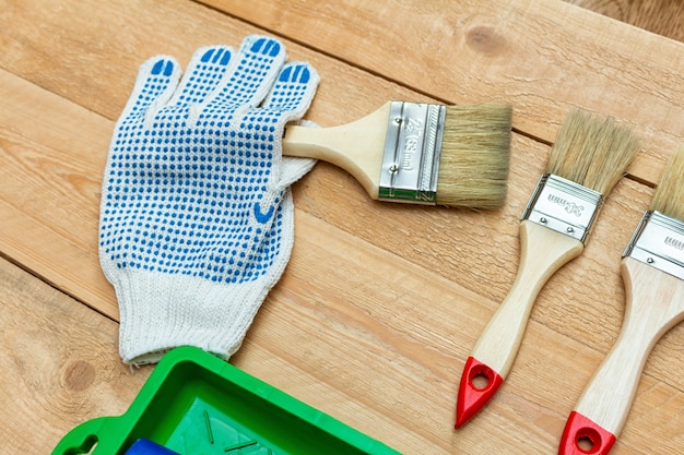 Composición de herramientas de pintura con pinceles, guantes y rodillo de pintura sobre el fondo de madera.