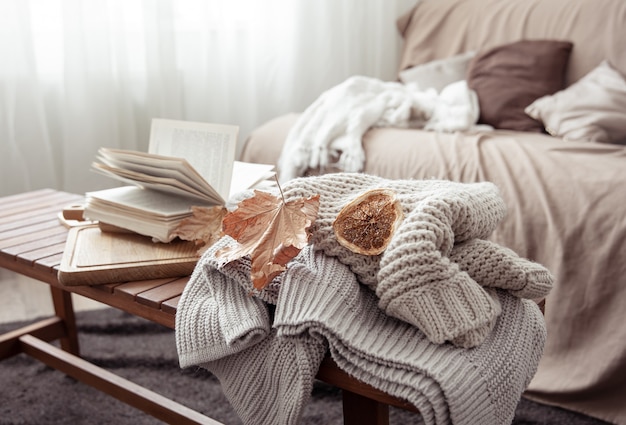 Una composición hogareña acogedora con un suéter de punto, un libro y hojas en el interior de la habitación.