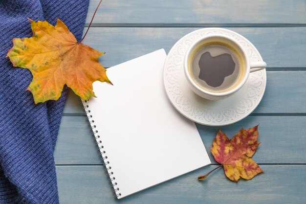 Composición con hojas de otoño cuadernos en blanco una taza de café en una mesa de madera azul