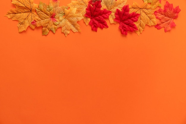 Composición con hojas de otoño falsas sobre fondo naranja