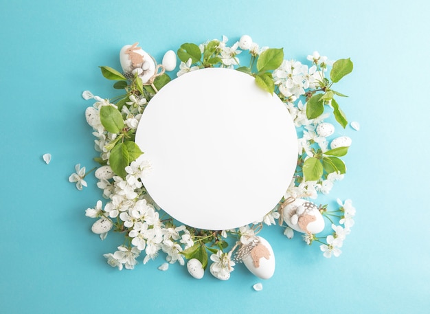 Composición de huevos florales de Pascua con papel en blanco redondo en el centro del fondo azul