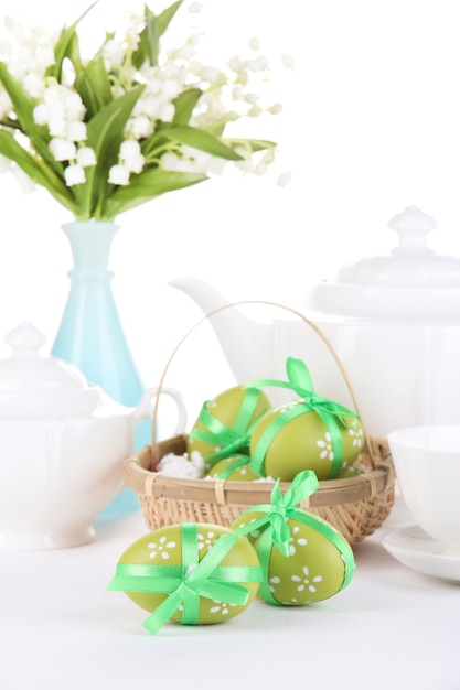 Composición con huevos de pascua en la canasta cerca de la tetera, la taza y el ramo de flores