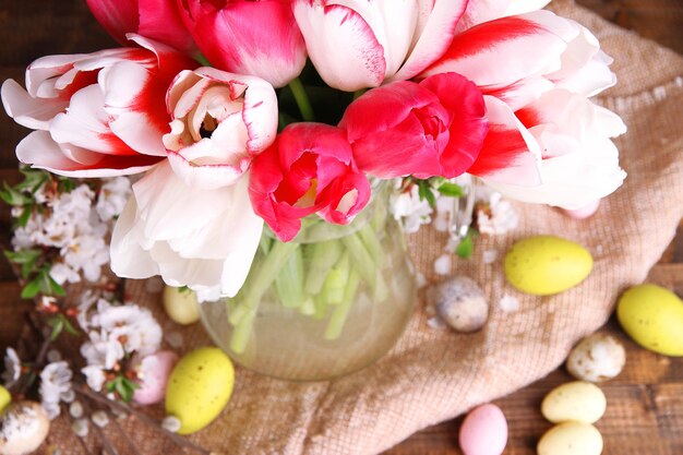 Composición con huevos de Pascua y hermosos tulipanes en jarra de vidrio sobre fondo de madera