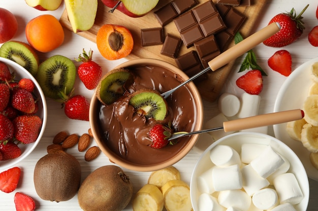 Composición con ingredientes para fondue de chocolate sobre fondo blanco de madera. Cocinar fondue