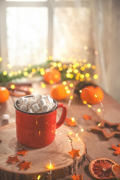 Composición de invierno acogedora y linda taza roja malvaviscos naranjas y luces de Navidad