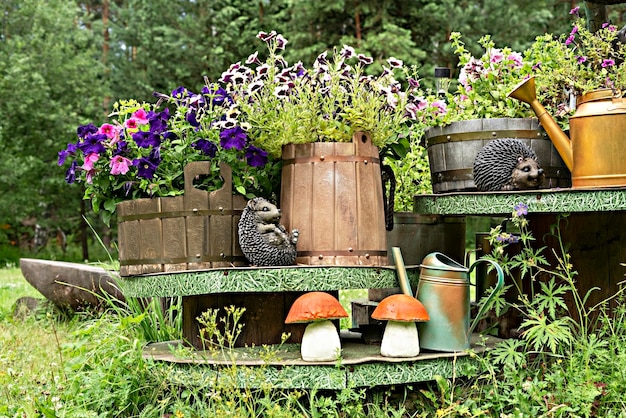 Composición de jardín hecha a mano de macetas de madera con petunias figuritas de cerámica de erizos y regaderas de setas