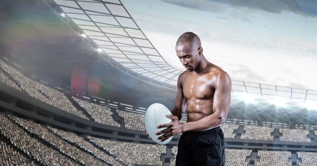 Composición del jugador de rugby masculino sin camisa sosteniendo una pelota de rugby sobre el estadio deportivo