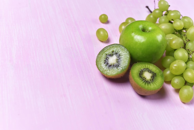 Composición de kiwi, uva y manzana sobre un fondo rosa