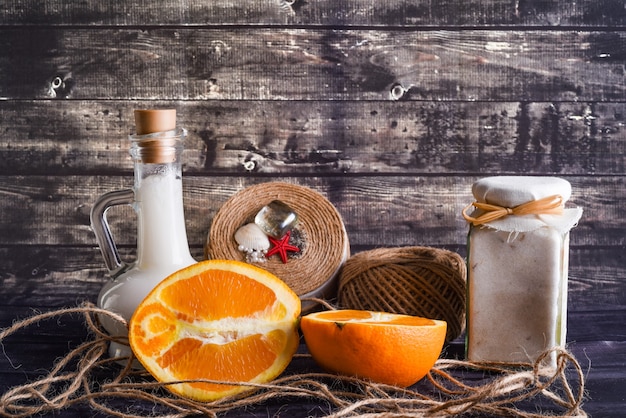 La composición laica con productos para el cuidado del cuerpo. un tarro de crema natural, una botella de aceite de coco y una naranja madura