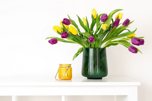 Composición mínima, estilo higiénico nórdico escandinavo, interior de la casa, tulipanes del día de la madre en florero verde, candelabro amarillo