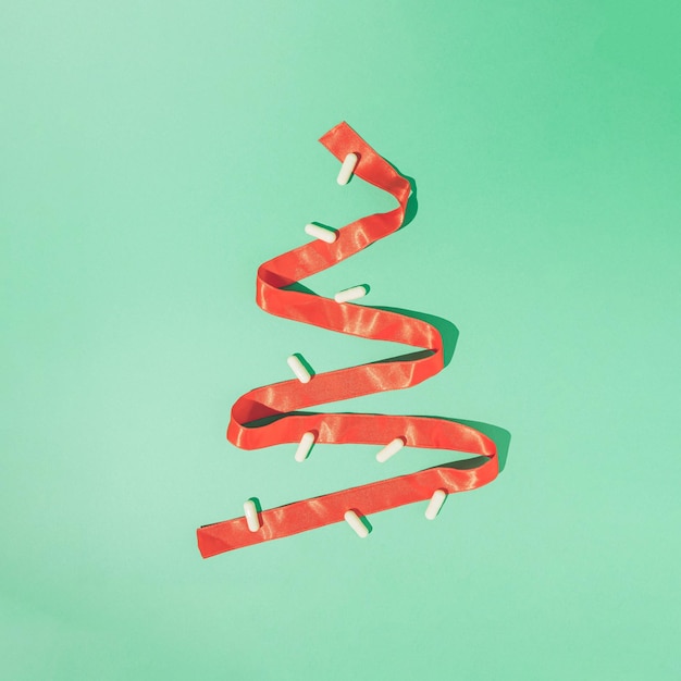 Composición mínima de invierno hecha de cinta de Navidad roja y pastillas blancas sobre fondo verde menta
