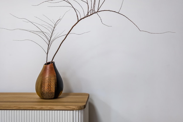 Foto composición minimalista de jarrón redondo con rama seca en la cómoda contra la decoración interior de la pared blanca