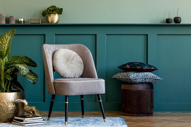 Composición moderna de salón con sillón de diseño gris, maceta dorada con hermosa planta, puf, almohadas y elegantes complementos personales. Revestimiento de pared con balda. Elegante puesta en escena en casa.