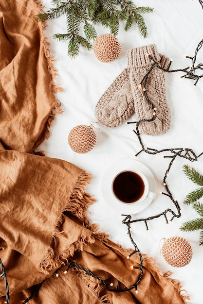 Composición de Navidad año nuevo. Mitones de punto, taza de café, guirnaldas, ramas de abeto, adornos navideños, cuadros de jengibre en manta blanca