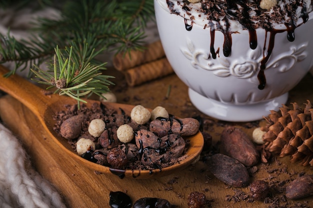 Composición de Navidad o año nuevo con bebida de chocolate caliente o cacao con crema batida servida con chocolate picado y granos de cacao en placa de madera rústica.