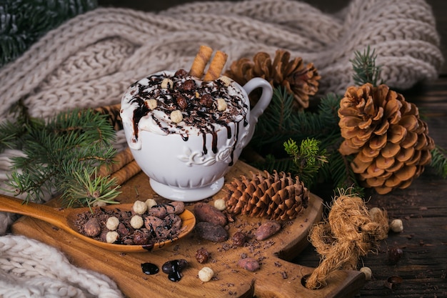 Composición de Navidad o año nuevo con bebida de chocolate caliente o cacao con crema batida servida con chocolate picado y granos de cacao en placa de madera rústica.