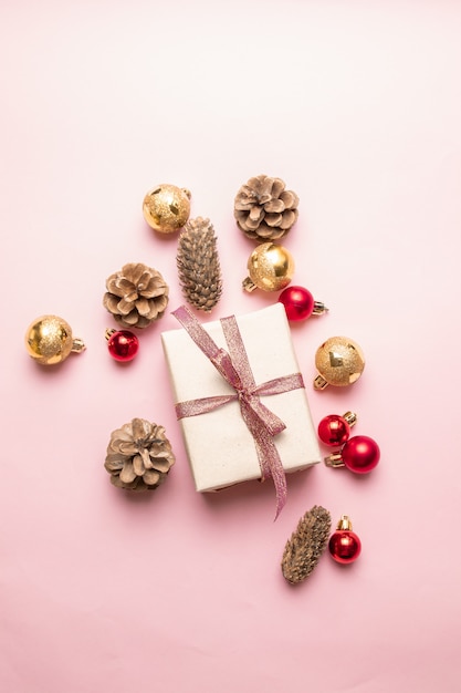 Composición de Navidad o año nuevo de caja de regalo con cinta roja, cono de pino, oro y bolas rojas en un rosa.