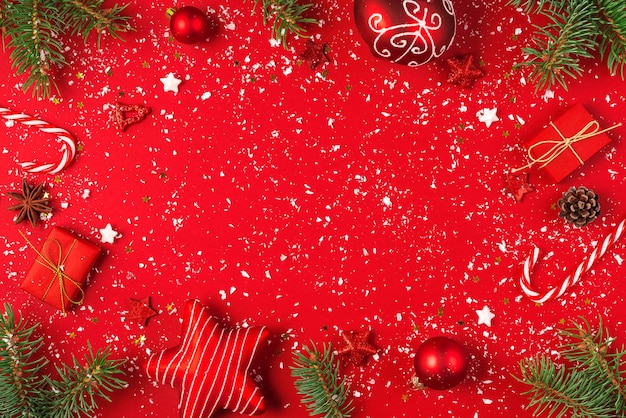Composición de Navidad o feliz año nuevo. Marco hecho de ramas de abeto, piñas y adornos navideños sobre fondo rojo cubierto de nieve. endecha plana. vista superior con espacio de copia