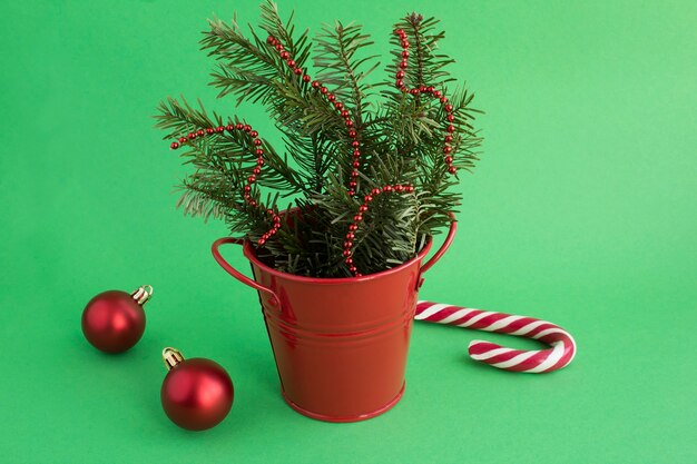 Composición de Navidad con ramas de abeto en el cubo rojo sobre fondo verde. Copie el espacio.