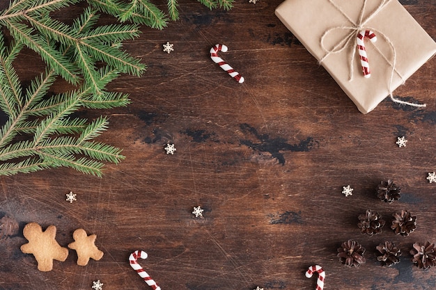 Composición de Navidad con regalo y hombre de pan de jengibre sobre fondo oscuro de madera con conos de pino, ramas de abeto en el escritorio de madera, vista plana y superior, espacio de copia
