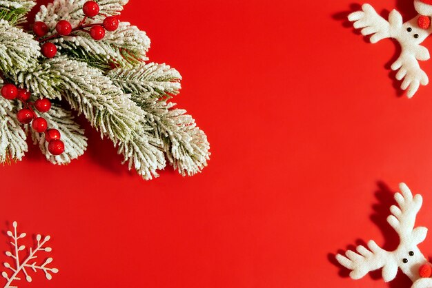 Composición de Navidad sobre fondo rojo de árbol de nieve con frutos rojos y ciervos decorativos. Endecha plana, vista superior, espacio de copia.