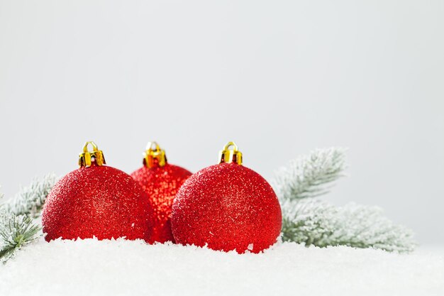 Composición navideña con adornos rojos y rama de abeto verde sobre fondo blanco de nieve