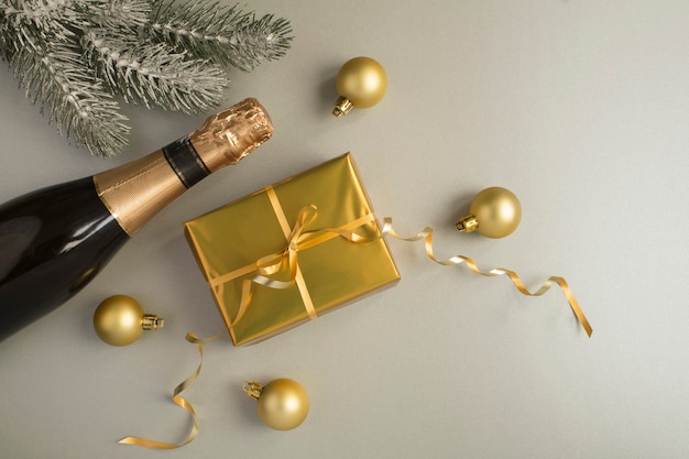 Composición navideña con botella de champán y caja de regalo dorada sobre fondo gris