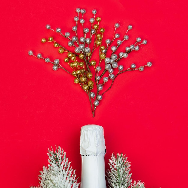 Composición navideña con botella de vino espumoso blanco y adornos navideños rojos en tarjeta roja