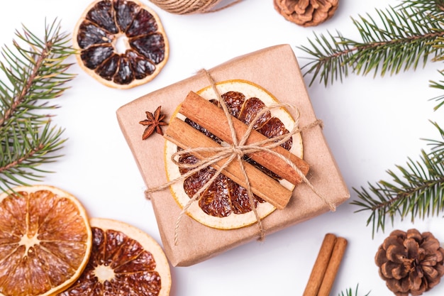 Composición navideña con caja de regalo de papel kraft hecho a mano, rodajas de cítricos secos, canela, anís, piñas y ramas de abeto, vista superior de cerca