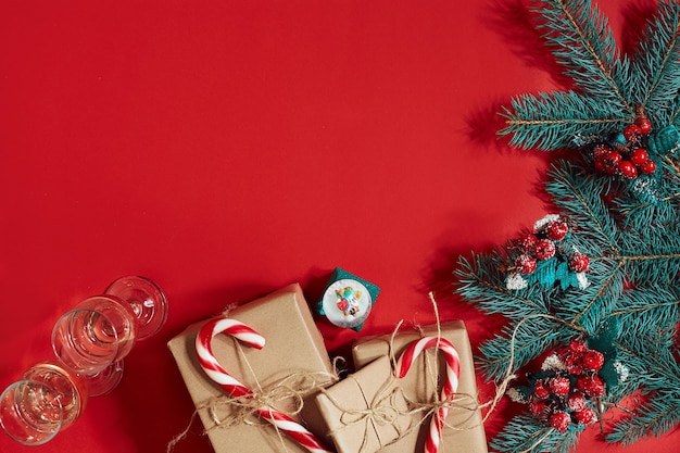 Composición navideña de conos de pino ramas de abeto y pila de cajas de regalo sobre fondo rojo.