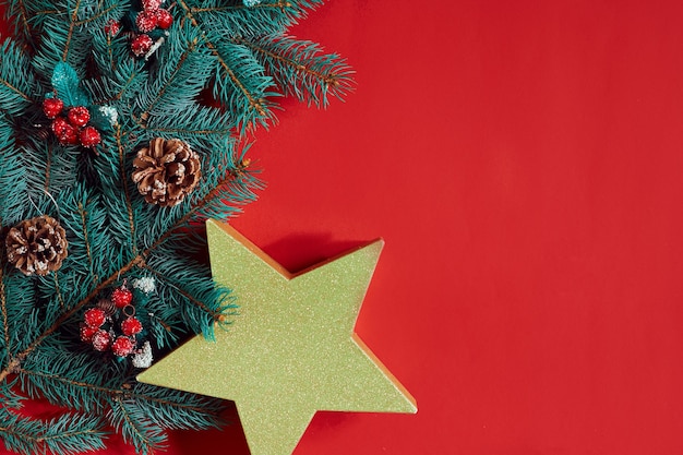 Composición navideña de conos de pino ramas de abeto y pila de cajas de regalo sobre fondo rojo.