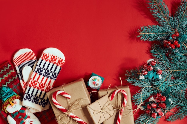 Composición navideña de conos de pino ramas de abeto y pila de cajas de regalo sobre fondo rojo.