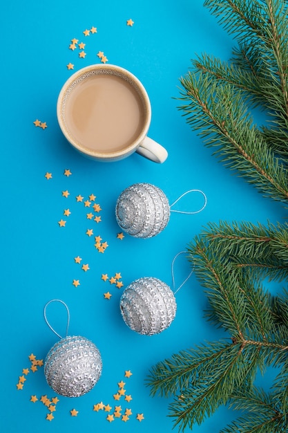 Composición navideña. Decoraciones, bolas de plata, ramas de abeto y abeto, taza de café sobre papel azul. Endecha plana.