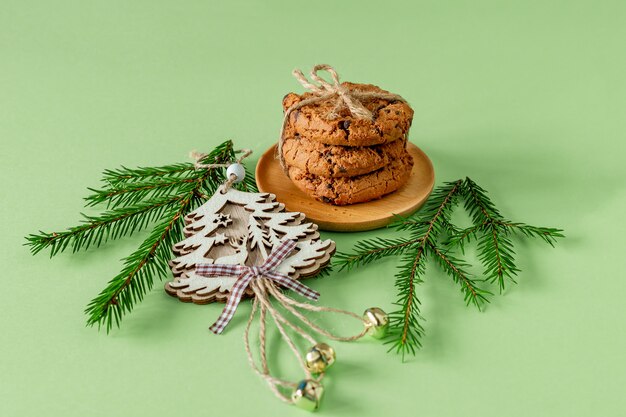 Composición navideña con galletas de chispas de chocolate sobre papel verde con ramas de abeto y juguete de madera. tarjeta de felicitación festiva.