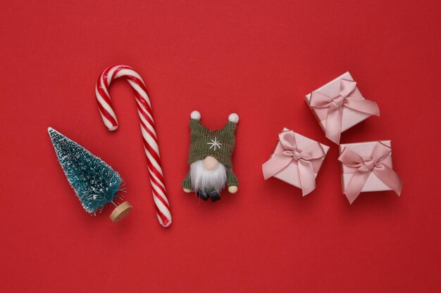 Composición navideña Gnomo de árbol de Navidad y cajas de regalo de bastón de caramelo sobre fondo rojo