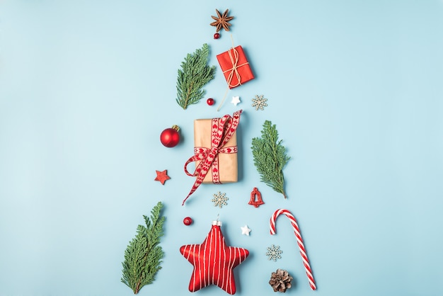 Composición navideña hecha de ramas de abeto, decoración, dulces, bayas y cajas de regalo sobre fondo azul.