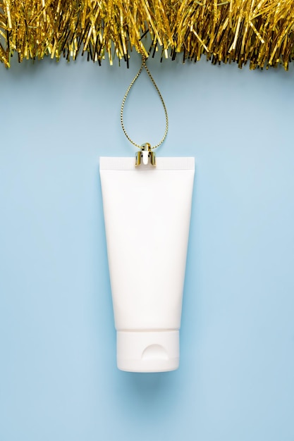 Composición navideña hecha de tubo de crema cosmética cinta dorada y oropel sobre fondo azul Maqueta de espacio de copia plana