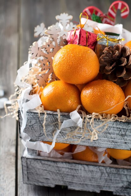 Composición navideña. Mandarinas frescas y juguetes de año nuevo en una caja en la madera vieja