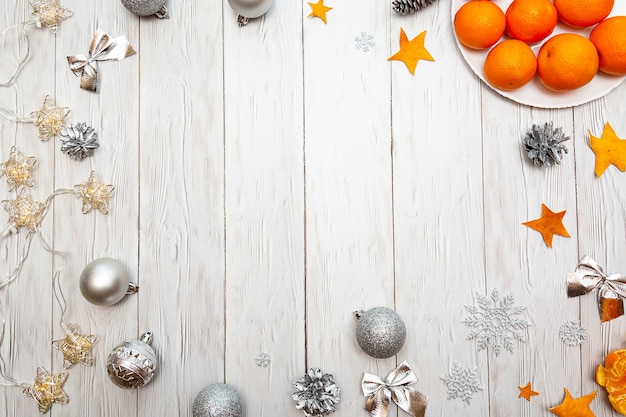 Composición navideña con mandarinas plateadas, adornos navideños y guirnaldas de luces sobre un blanco