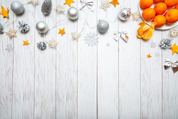 Composición navideña con mandarinas plateadas, adornos navideños y guirnaldas de luces sobre un blanco