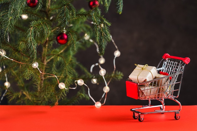 Composición navideña. Mini carro con cajas de regalo cerca de un árbol de Navidad con juguetes