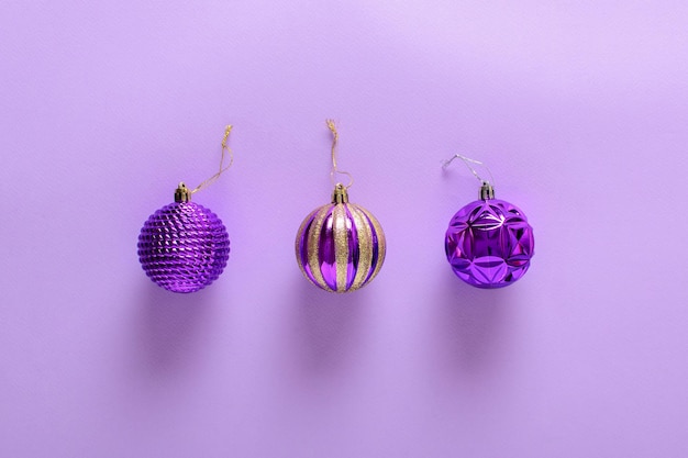 Composición navideña con tres bolas de árbol de Navidad moradas sobre un fondo morado claro