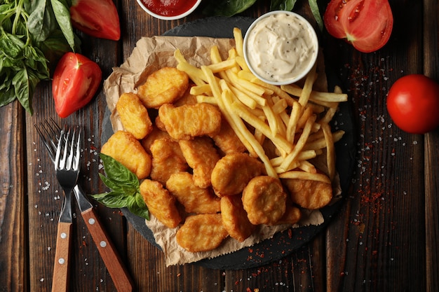 Composición con nuggets de pollo, salsas y patatas sobre fondo de madera