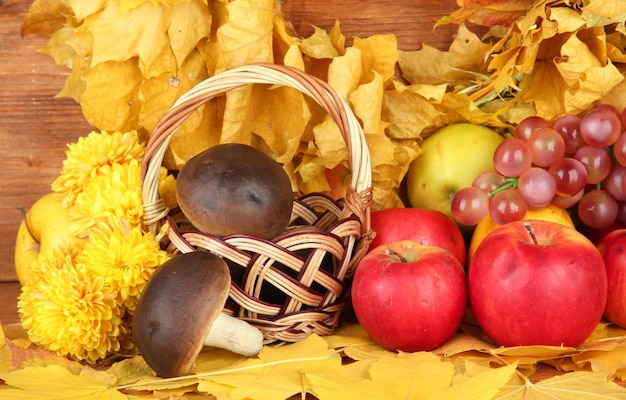 Composición otoñal con hojas amarillas, manzanas y champiñones sobre fondo de madera