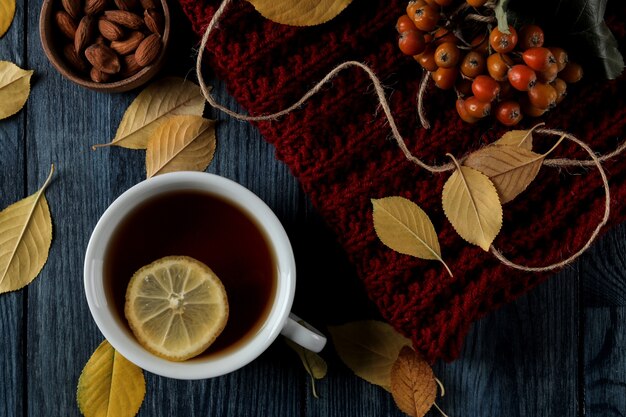 Composición otoñal con té caliente nueces bayas y hojas amarillas otoñales sobre una mesa de madera azul oscuro. vista superior