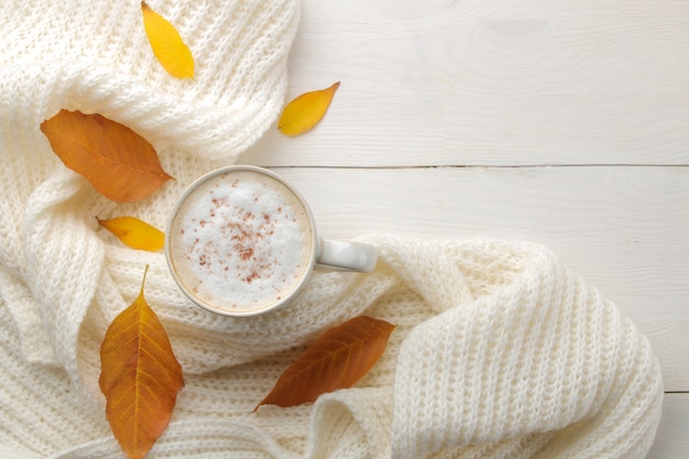 Composición de otoño con café caliente, una bufanda cálida y hojas amarillas sobre una mesa de madera blanca. vista superior con espacio para inscripción