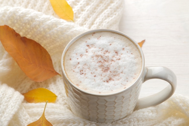 Composición de otoño con café caliente, una bufanda cálida y hojas amarillas sobre una mesa de madera blanca