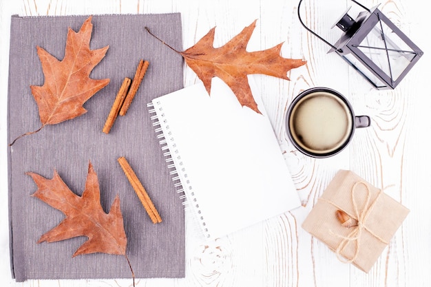 Composición de otoño con diario vacío taza de café hojas secas de otoño regalo de linterna envuelto en papel kraft sobre fondo rústico de madera blanqueada Espacio de copia plana